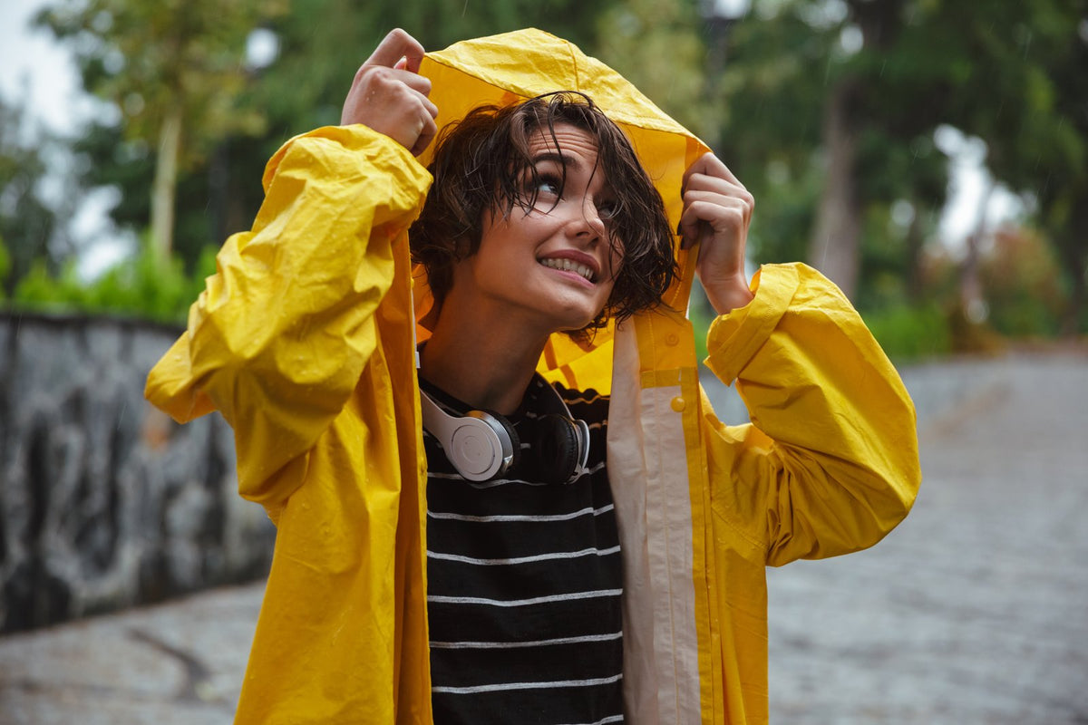 Smiling person in yellow raincoat looking up at the rain — the sunshine vitamin
